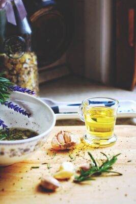 A rustic kitchen setup featuring olive oil, garlic, and herbs on a wooden board.