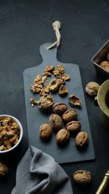 A vertical shot of whole and cracked walnuts on a dark wooden cutting board, perfect for food enthusiasts.