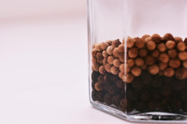 Macro shot of mixed peppercorns in a clear jar, showcasing texture and color contrast.