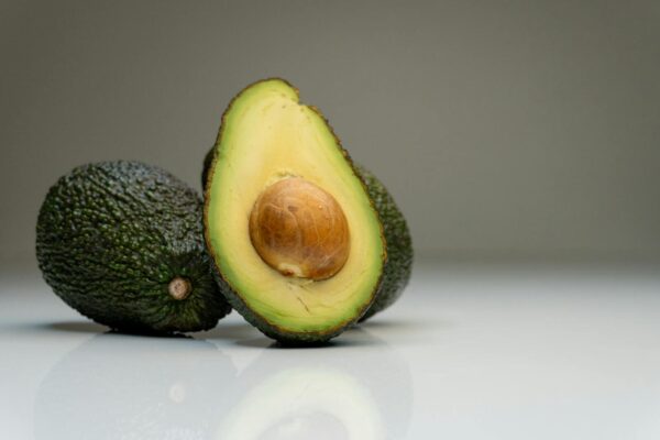 Close-up of ripe avocados with a sliced half showing the seed, against a gray background.