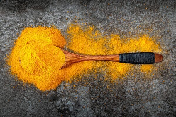 Vibrant turmeric powder spread with a wooden spoon for cooking inspiration.
