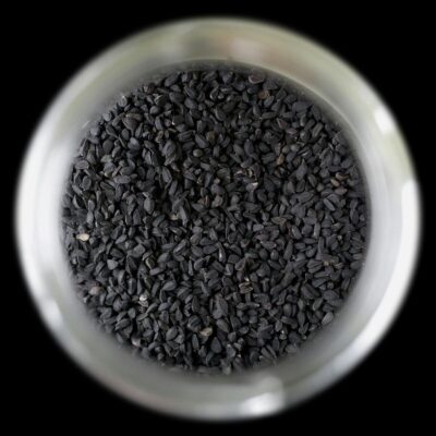 A close-up, top view of black cumin seeds (Nigella sativa) stored in a glass jar.