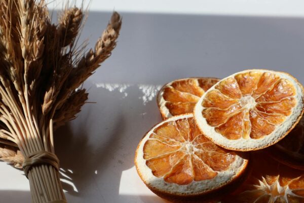 Mutfak Kültüründe ve Gastronomide Yeni Bir Soluk: Portakal Kurusu Rehberi Atmospheric composition of sunlit dried orange slices and wheat bundle casting shadows.
