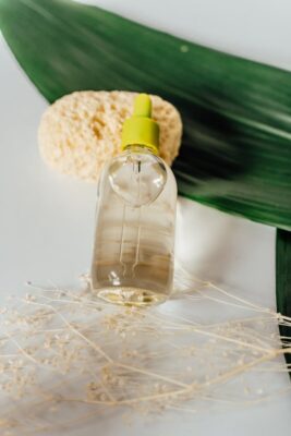 Esansiyel yağ içeren cam bir şişenin yakın çekim görüntüsü; etrafı yapraklar ve sünger gibi doğal unsurlarla çevrili.