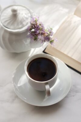 From above porcelain cup of hot black coffee placed next to notebook with blank pages and sugar bowl on table with light surface