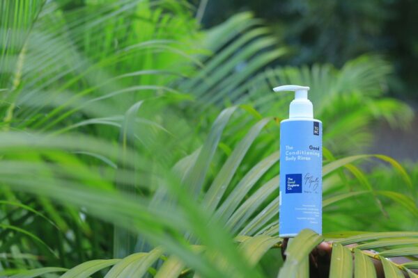 A bottle of lotion sits among green leaves.