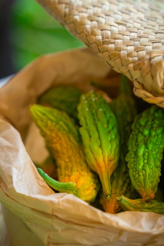 Close-up of vibrant green bitter melons in a rustic woven basket, showcasing a healthy vegetable choice.