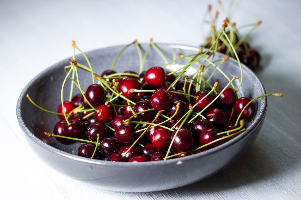 A close-up of fresh cherries in a grey bowl on a light background.