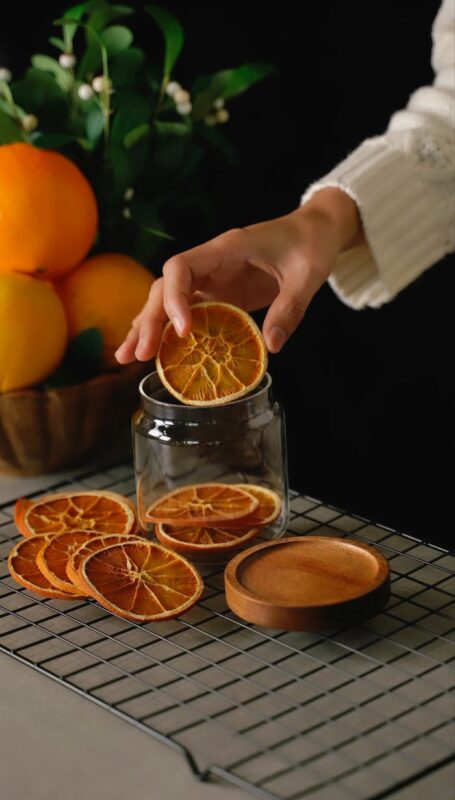 Mutfak Kültüründe ve Gastronomide Yeni Bir Soluk: Portakal Kurusu Rehberi A woman placing dried orange slices into a jar on a cooling rack for food preparation.