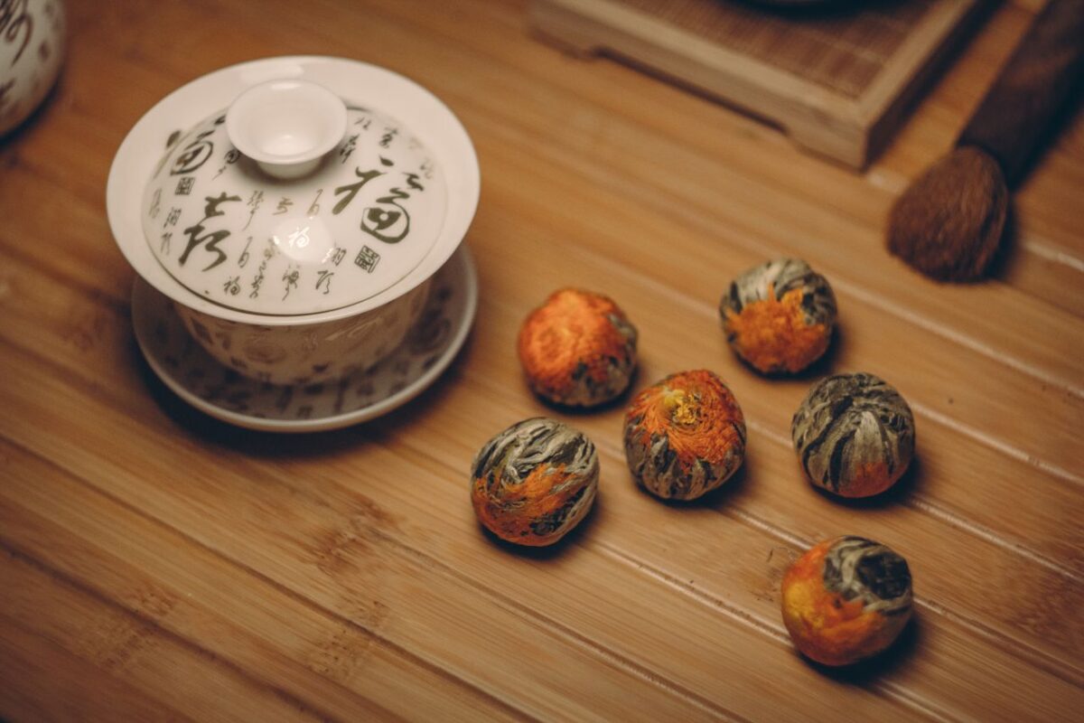 Stylish Chinese tea set with blooming tea balls on bamboo surface, capturing serene tea culture.