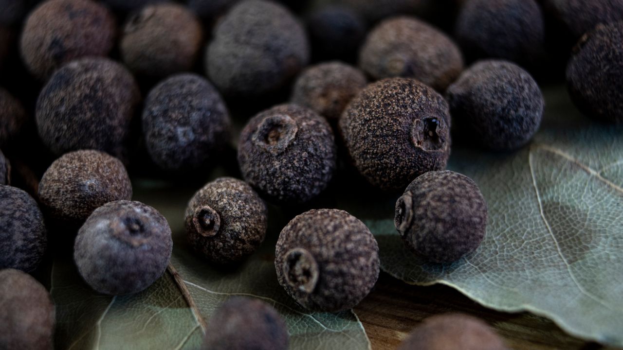A macro shot of dried allspice berries scattered over fresh bay leaves, highlighting their texture.