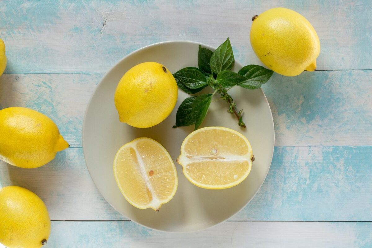 Limon Kabuğu Yağı: Doğadan Gelen Ferahlığın ve Saf İçeriğin Hikayesi Top-down view of lemons with fresh green leaves on light wooden background.