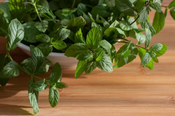 Close-up of fresh mint leaves in a bowl on a wooden surface, top view.