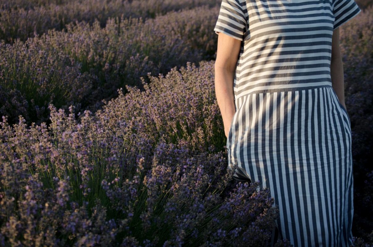 A woman in a striped dress stands amidst a serene lavender field during sunset.